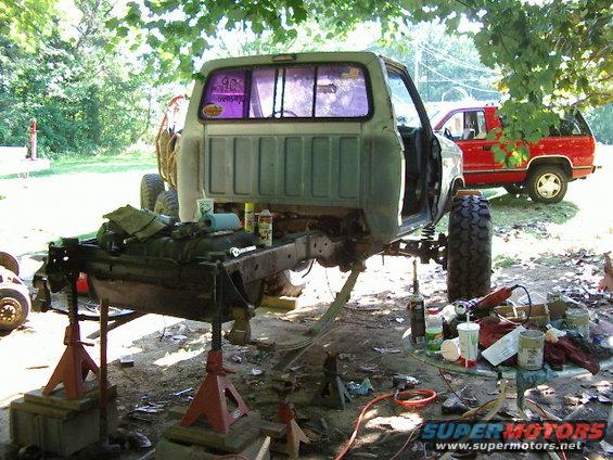 Pickup truck body on jack stands, rear view. Another red truck in background