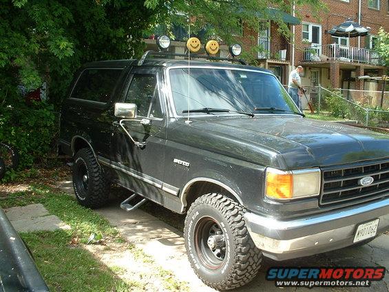 1989 Ford Bronco parked on a driveway with trees and a brick building in the background