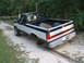 1989 Ford F-150 - A two-tone Ford pickup truck is parked on a dirt road with its rear passenger-side wheel missing.