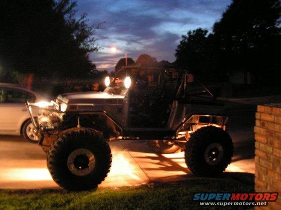 Off-road vehicle with large tires and roll cage, side view at dusk