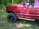 1994 Ford Bronco - A red Ford Bronco is parked off-road, showing its side profile and off-road tires.