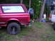 1994 Ford Bronco - A red SUV is parked in a wooded area next to a campfire scene with people gathered.
