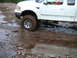 1994 Ford Bronco - This pickup truck is stuck in the mud, with its front tire submerged in water and mud.