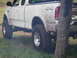 1994 Ford Bronco - Muddy pickup truck with 4x4 badging parked near a tree.