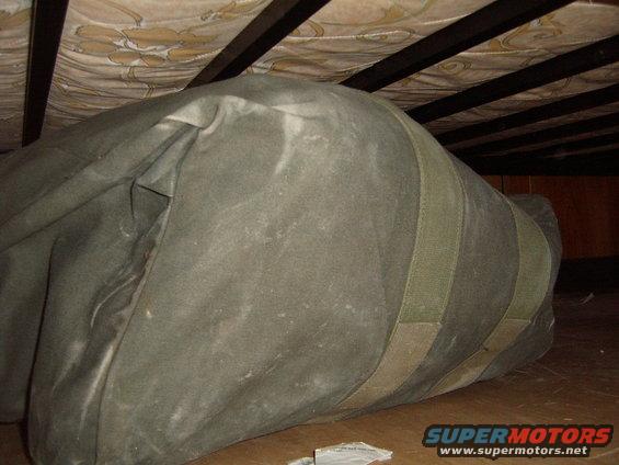 Large green duffel bag stored under a bed frame with wooden slats