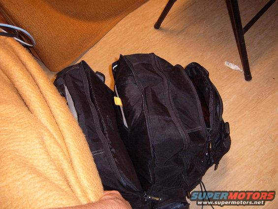 Black backpack with zippers open, sitting on a wooden floor next to an orange blanket