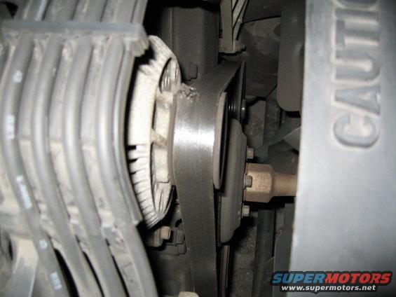 Close-up of car's alternator and drive belt system. Some spark plug wires are visible on the left