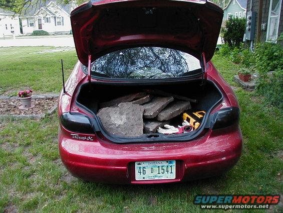 Red 1997 Ford Taurus rear view with open trunk carrying stones and tools