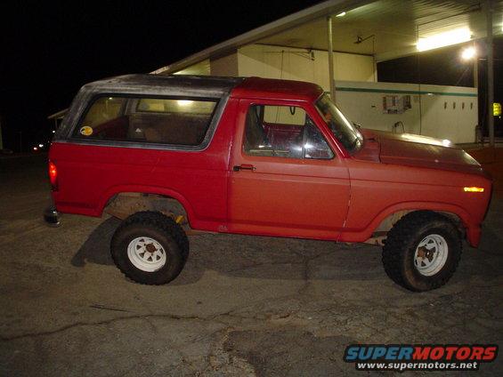 Red SUV parked at night, looks like a Ford Bronco from the early 80s