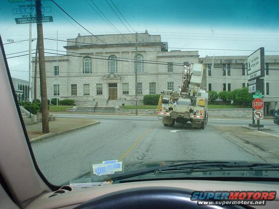 Utility truck with a boom lift, seen from behind on a street in front of a large building