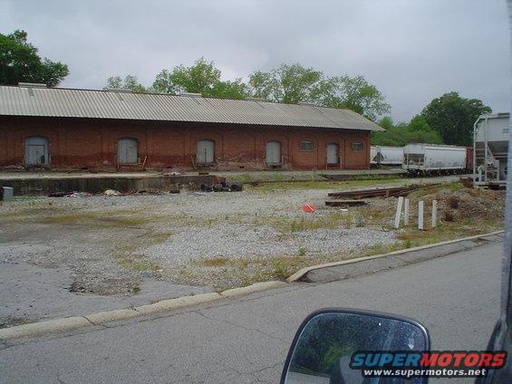 Several white railroad cars parked next to a long brick building with a metal roof