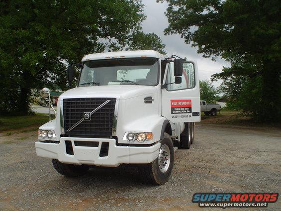 White Volvo truck with open driver's door, parked on gravel lot