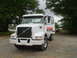 1981 Ford Bronco - A white Volvo truck is parked on a gravel lot with trees in the background.