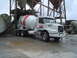 1981 Ford Bronco - A white concrete mixer truck is parked on wet ground next to industrial silos.
