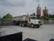 1981 Ford Bronco - A white Volvo dump truck and trailer are parked at a gravel pit with industrial silos in the background.