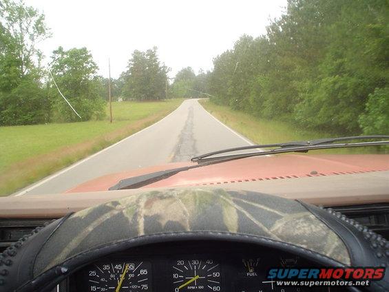 Dashboard view of a road ahead, with gauges visible. Camo steering wheel cover