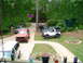 1981 Ford Bronco - Multiple vehicles are parked in a driveway surrounded by trees and greenery.
