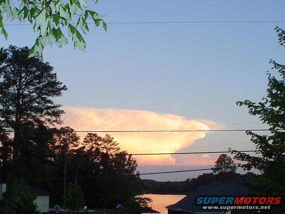 Sunset sky with large cloud formation over a lake and trees