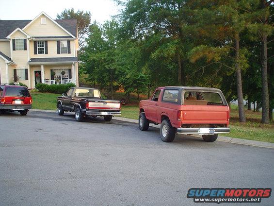 Red Ford Bronco and black Ford pickup truck parked on street in front of house