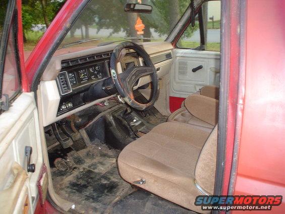 Interior of a red truck with tan seats and a dirty floor. The dashboard shows gauges and a steering wheel