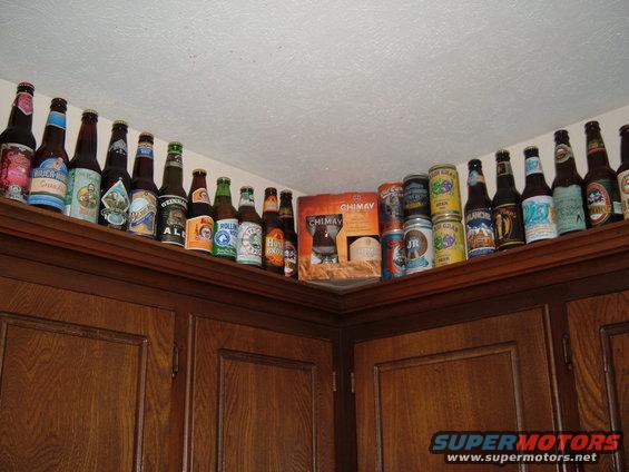 Various beer bottles and cans displayed on a shelf above kitchen cabinets