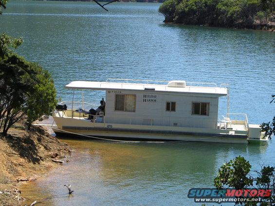 Houseboat named Holiday Harbor docked near a wooded shore on a lake