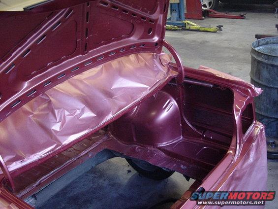 Maroon car trunk interior with plastic sheeting, showing structural details and a spare tire well