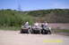 2003 Honda RUBICON - Three people ride ATVs on a dirt path with a wooded hillside behind them.