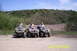 2003 Honda RUBICON - Three men on ATVs pause on a dirt path with a wooded hill in the background.