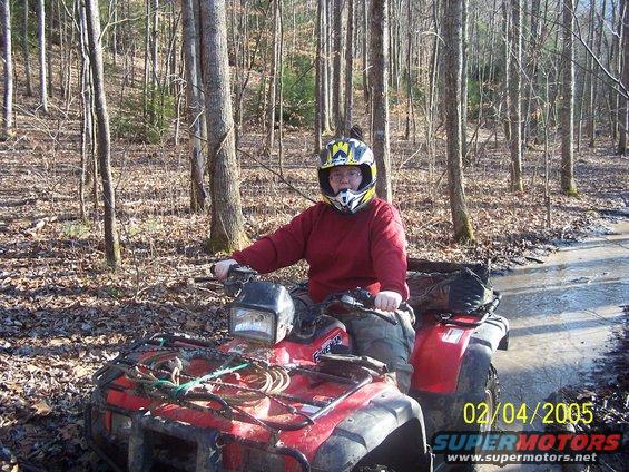 Person wearing a helmet on a red ATV, riding through a muddy wooded trail. Date stamp reads 02/04/2005
