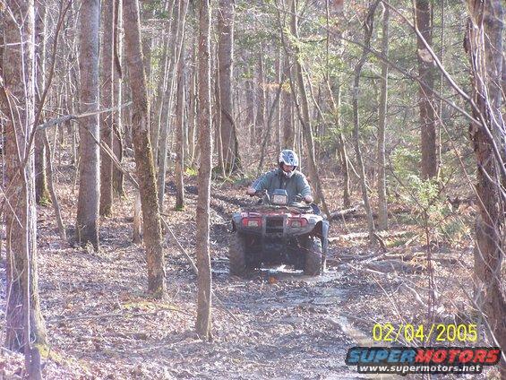 guy on red ATV riding on muddy trail in woods