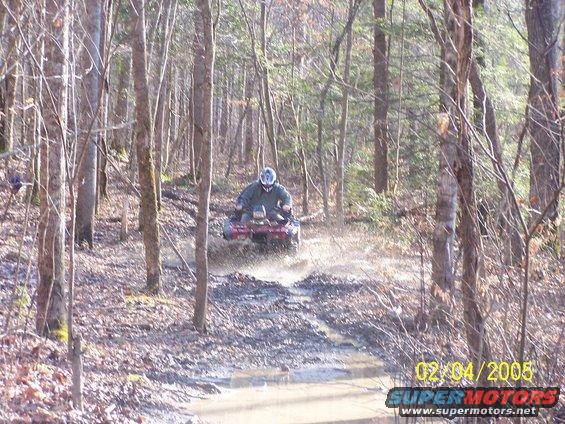 Red ATV splashing through mud on a wooded trail