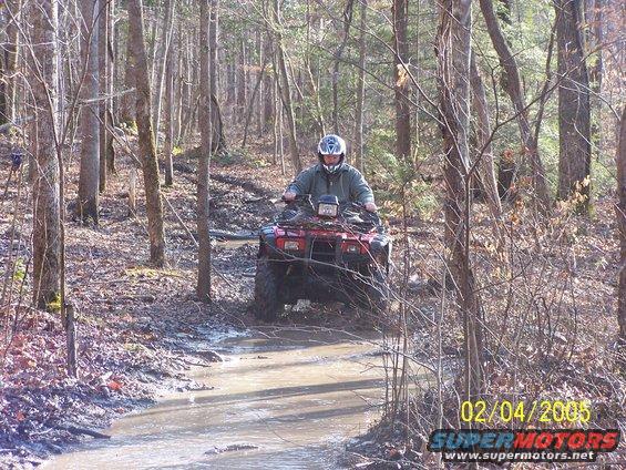 Person riding red ATV through a muddy wooded area