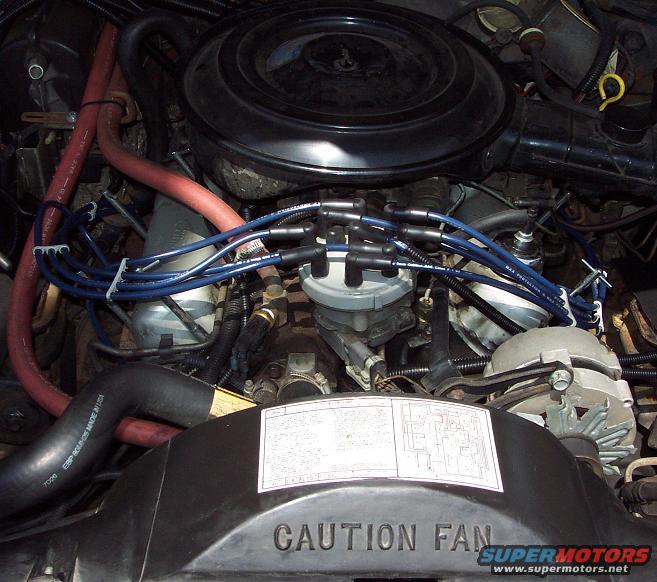 Engine bay of a 1985 Ford Crown Victoria LTD, showing the distributor, spark plug wires, alternator, and air cleaner. The engine appears to be in good condition