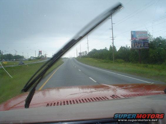 View from inside a vehicle looking out the windshield at a highway on a rainy day. Dashboard and windshield wipers are visible