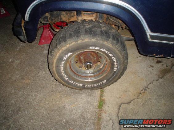 Close-up of a blue Ford Bronco's front wheel and fender, which is on a jack. BFGoodrich tires are visible
