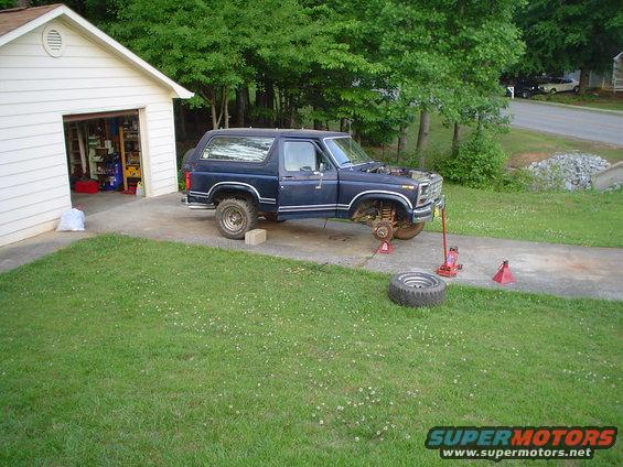 Dark blue 1981 Ford Bronco with hood open, front wheel removed, on jack stands