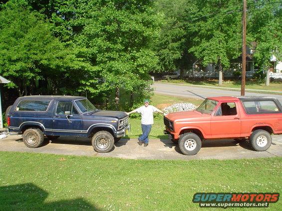 Guy between blue and orange Ford Broncos. The blue one has a spare tire on the back