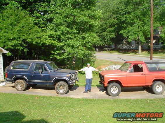 Two Ford Broncos, one blue and one orange, with a man standing between them