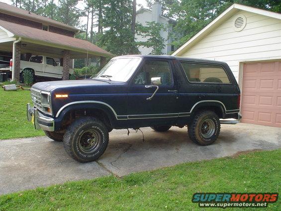1981 Ford Bronco parked in driveway next to a garage. White Ford pickup truck visible under carport
