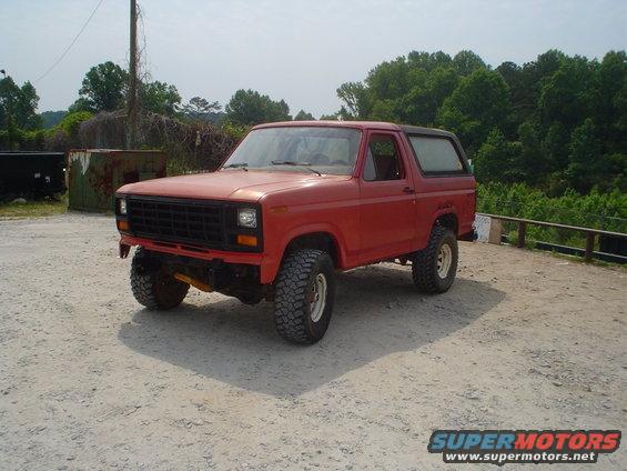 red Ford Bronco with aftermarket wheels and tires, parked on dirt