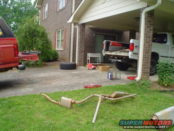 red pickup truck with camper shell, white pickup truck in driveway, exhaust system on grass