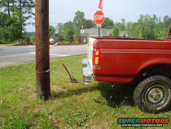 Red pickup truck rear with tow strap attached to a utility pole