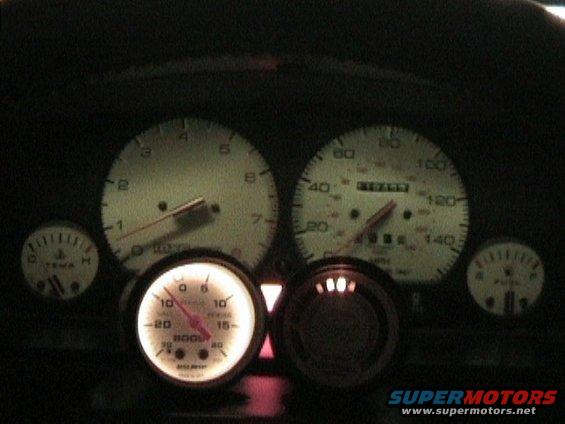 Car dashboard with illuminated gauges including speedometer, tachometer, boost, fuel, and temperature