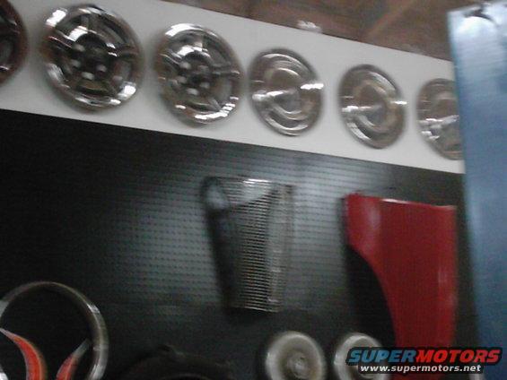 Collection of hubcaps and car parts including a red fender and a grille