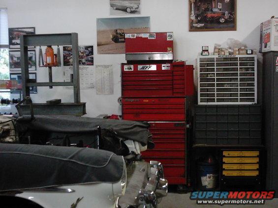 Garage interior with red tool chests, storage bins, and a covered vehicle in the foreground