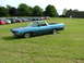 1970 Ford Ranchero - A blue 1970 Ford Ranchero is parked on a grassy field, with a building and a parking lot full of cars in the background.