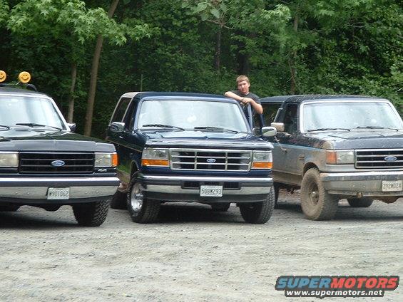 Three Ford Broncos parked on gravel, one blue, one black, one dark gray. 1989 Ford Bronco