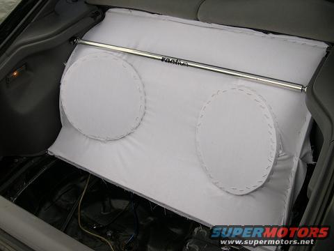 Custom white subwoofer box with two speakers and a metal brace inside a car's trunk