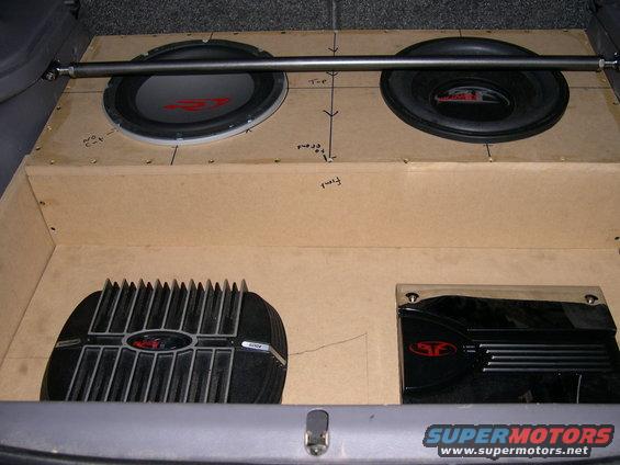 Car interior with custom wooden enclosure holding two subwoofers and two amplifiers